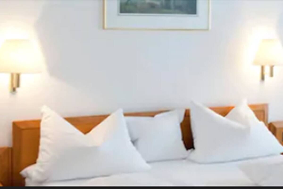 A hotel room with a bed, two bedside lamps, a framed picture on the wall, and a nightstand with a phone.
