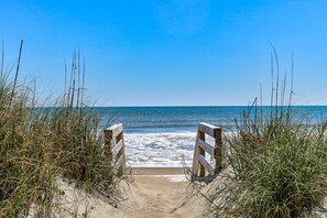 A beach entrance with wooden railings and sand leading to the ocean.