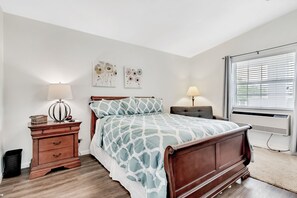 Quarto com cama, mesas de cabeceira, decoração na parede e janela com persianas.