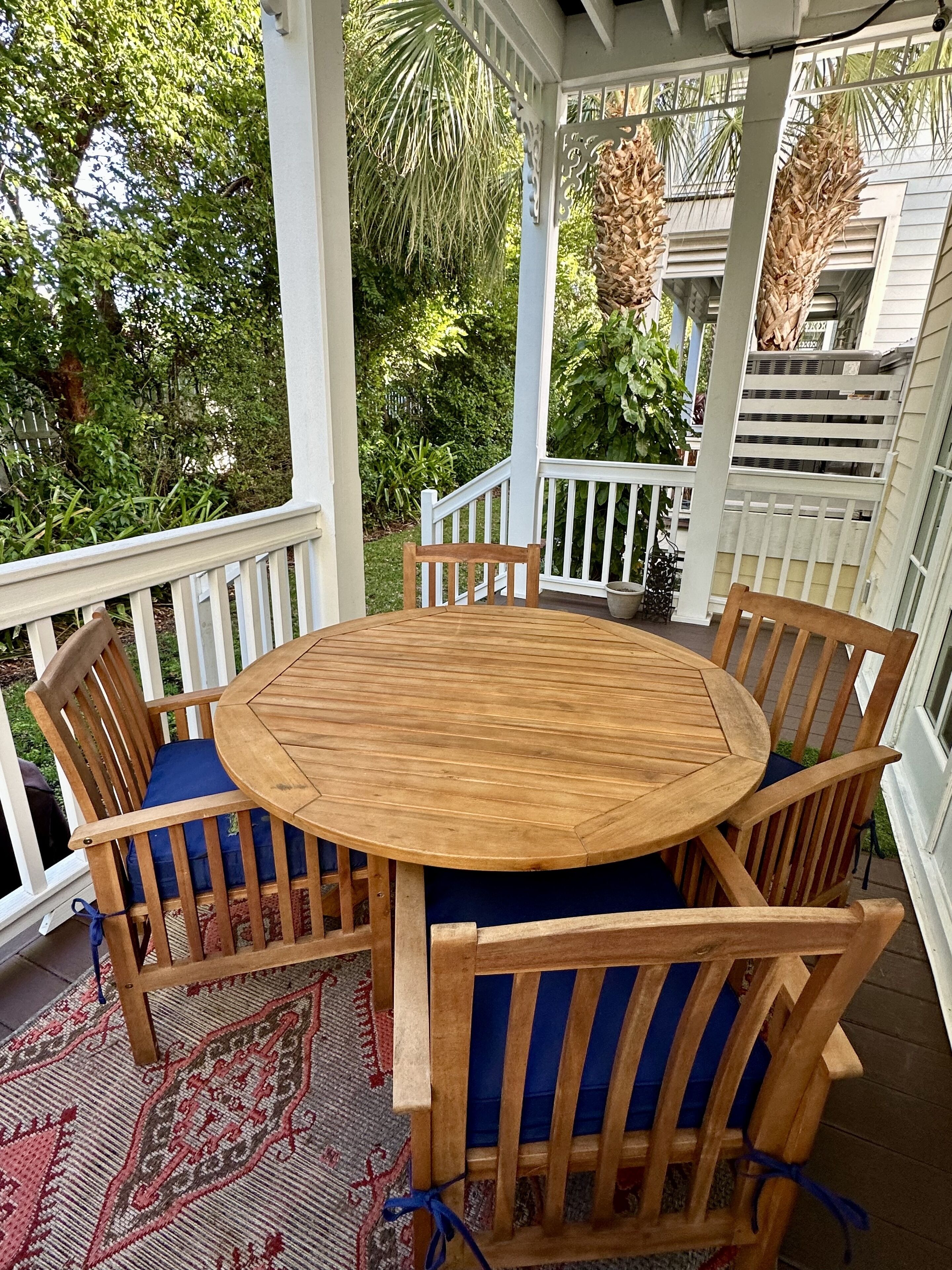 Une terrasse extérieure couverte, avec une table ronde en bois et six chaises en bois dotées de coussins bleus.