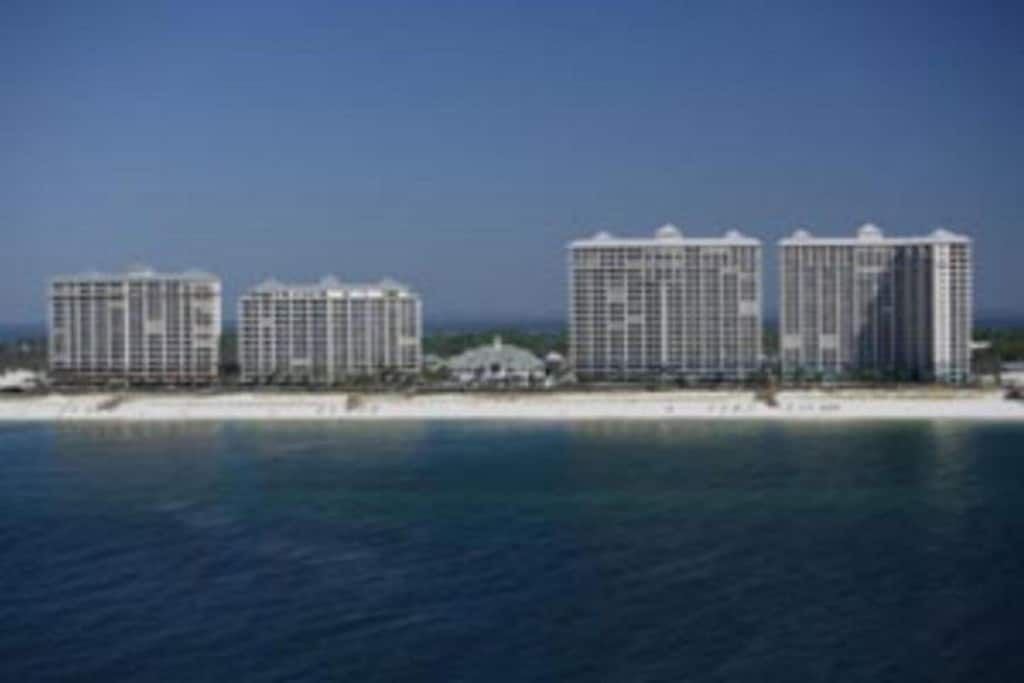 Un hotel costero con varios edificios de gran altura, una playa en primer plano y un cielo azul despejado.