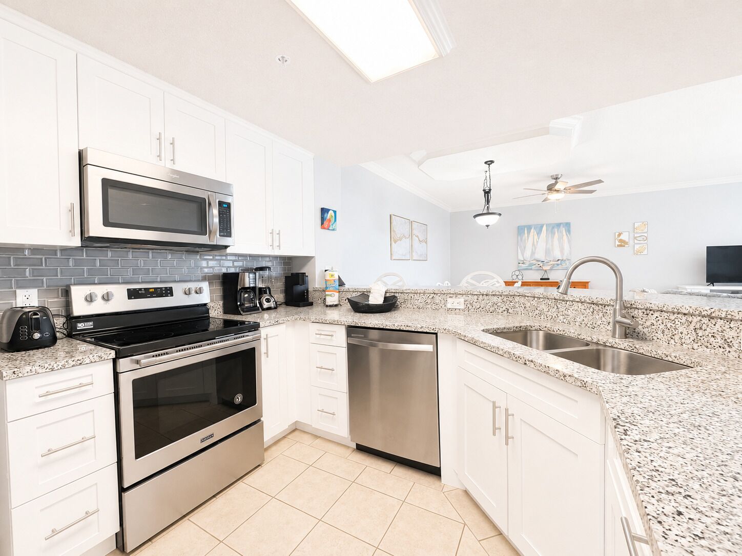 A modern kitchen with white cabinets, stainless steel appliances, a granite countertop, and a ceiling fan.