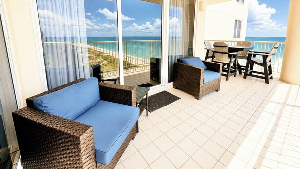 Ein Balkon mit Rattanmöbeln, einem Tisch und Stühlen mit Blick auf einen Strand.