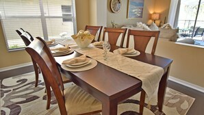 A dining area with a wooden table set for six, including plates, glasses, and a centerpiece. - Beautiful Pool Home With Kid's Play Room - Close to Theme Parks & Attractions (Kissimmee)
