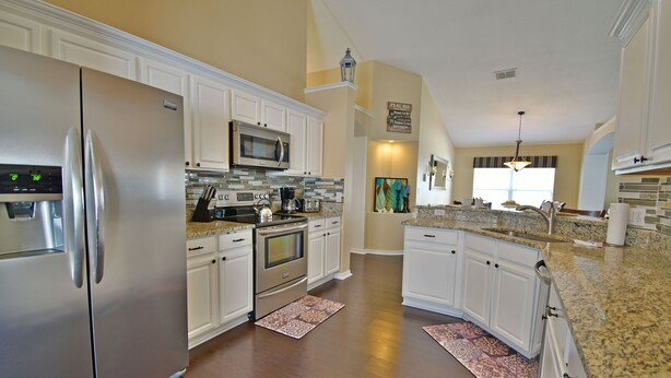 A modern kitchen with white cabinetry, stainless steel appliances, and a granite countertop. - Beautiful Pool Home With Kid's Play Room - Close to Theme Parks & Attractions (Kissimmee)
