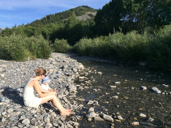 Iemand zit op een rotsachtige oever van een rivier, met een beboste heuvel op de achtergrond.