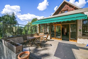 A wooden deck with outdoor furniture, a covered patio area, and a glass door entrance. - Hôtel Le Vieux Tilleul (Seyne)