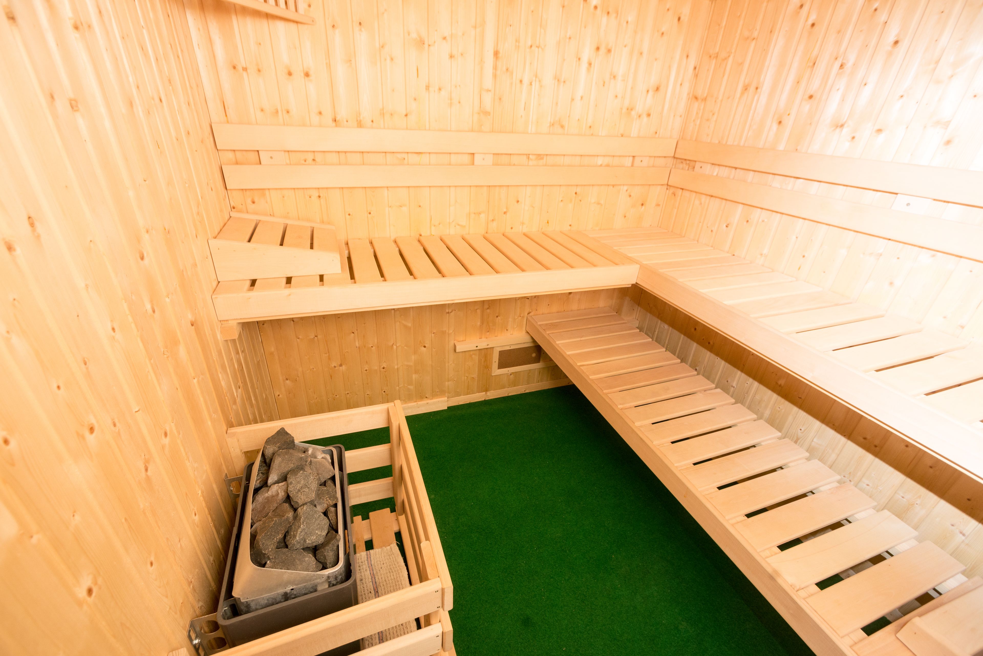 A sauna with wooden benches and a green floor.