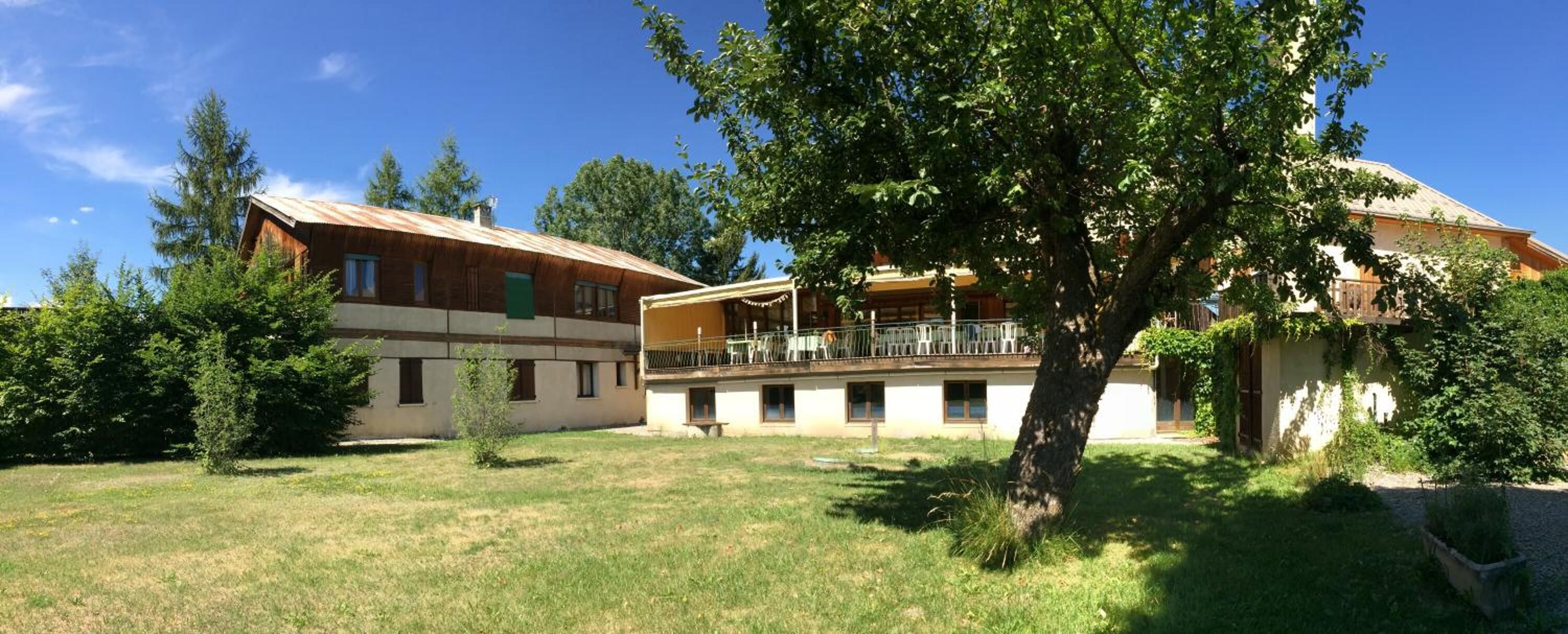 A two-story building with a balcony, surrounded by trees and a grassy lawn.