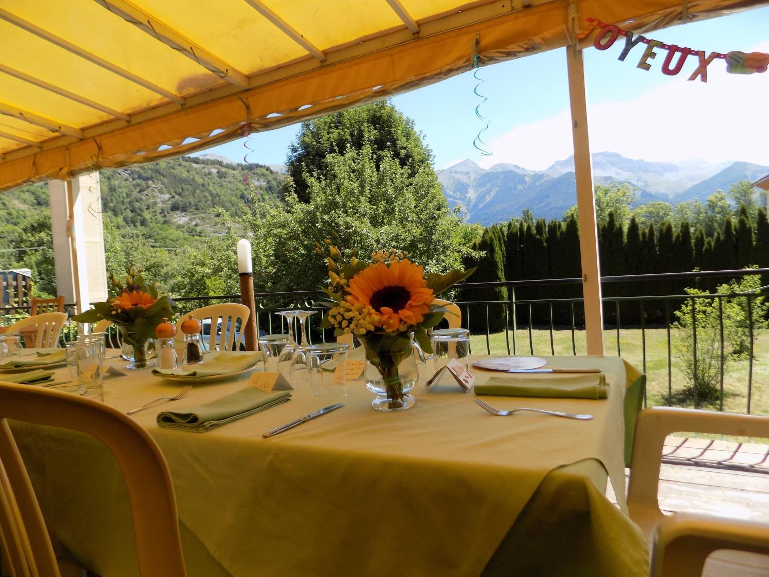 An outdoor dining area with a yellow tablecloth, sunflowers, and a view of mountains.