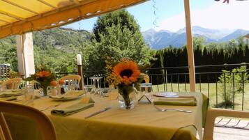 An outdoor dining area with a yellow tablecloth, sunflowers, and a view of mountains.