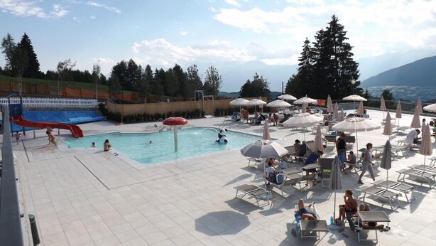 Zona de piscina con tobogán, sillas de descanso, sombrillas y vistas a montañas.