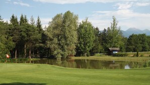 Un campo de golf con un estanque, árboles y un edificio pequeño al fondo.