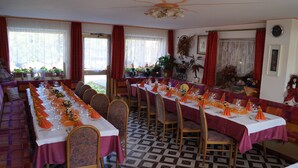 Un comedor con mesas largas dispuestas para una comida, sillas y un suelo estampado.