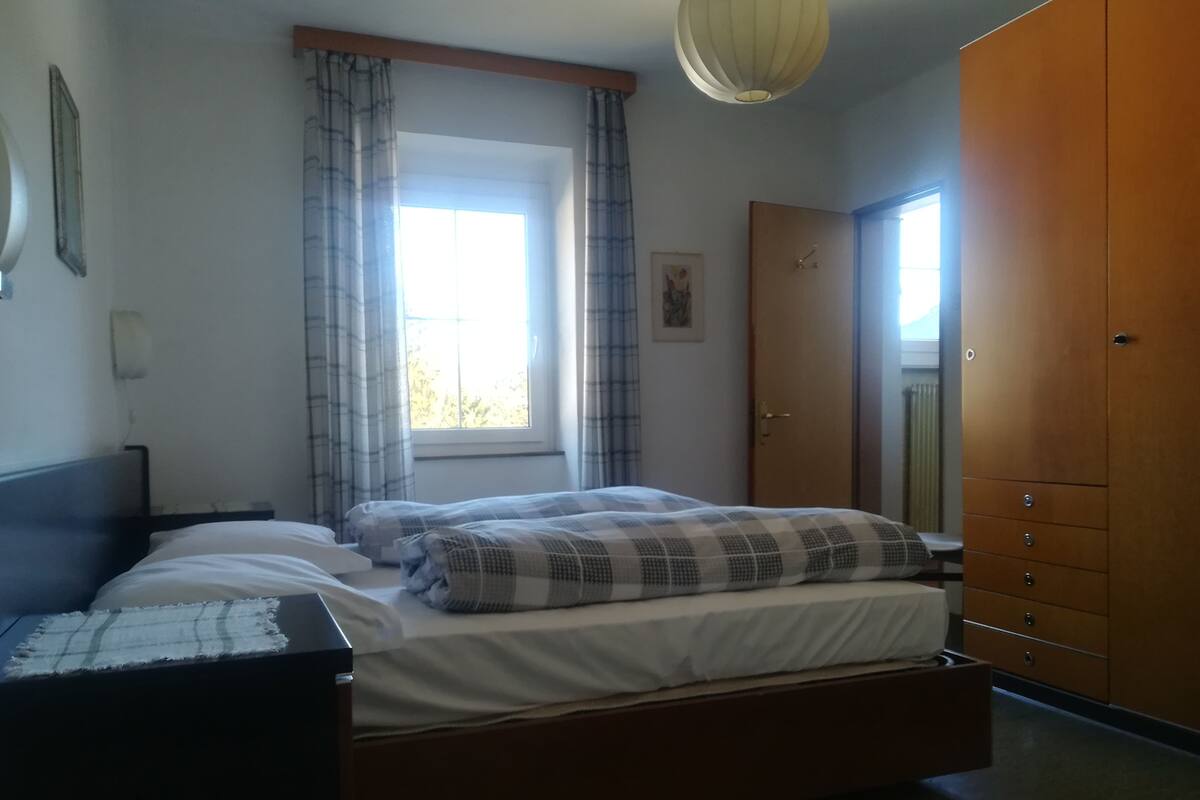 A bedroom with a bed, a wardrobe, a window with curtains, and a ceiling light.