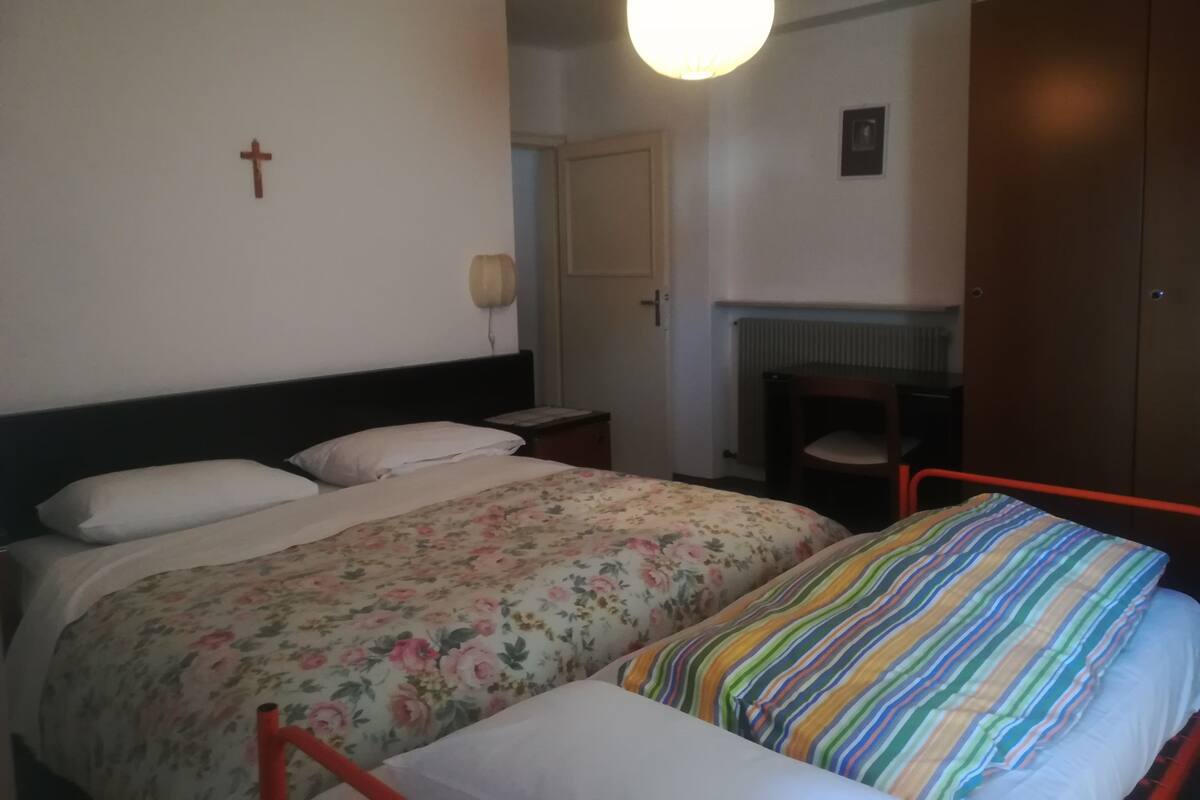 A bedroom with a bed, a chair, a wardrobe, and a wall-mounted light fixture.