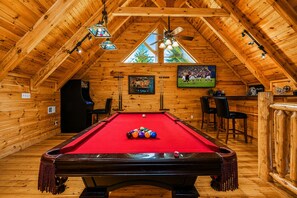 A wooden interior with a pool table, ceiling fan, and bar area.