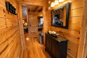 A wooden interior with a hallway leading to a bedroom, a dresser with decorative items, and a mirror on the wall. - Creating Memories-Theater Room, Wet Bar, Arcade, Hot Tub, Pool Table & Fire Pit (Sevierville)