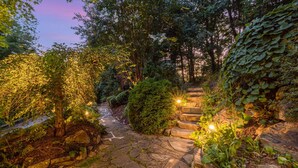 Een pad van stenen dat door een tuin met diverse planten en bomen loopt, verlicht door warme lichten.