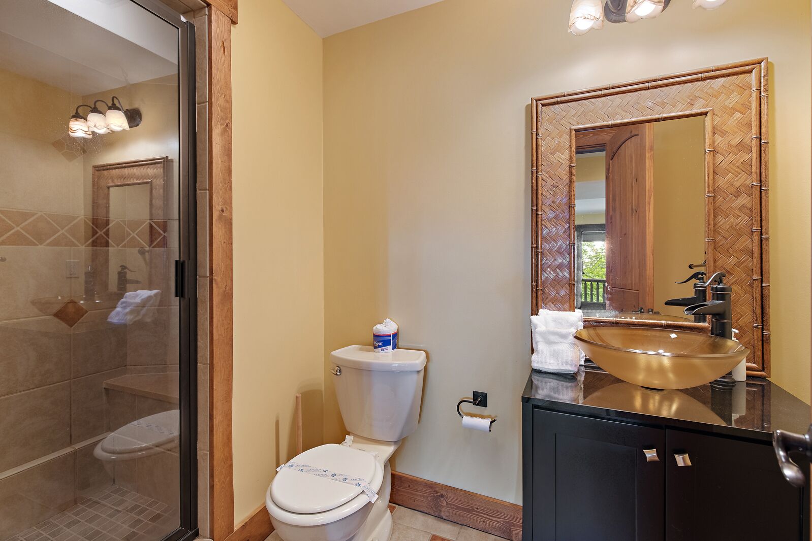 A bathroom with a glass shower enclosure, a toilet with a toilet paper holder, a sink with a mirror, and a cabinet.