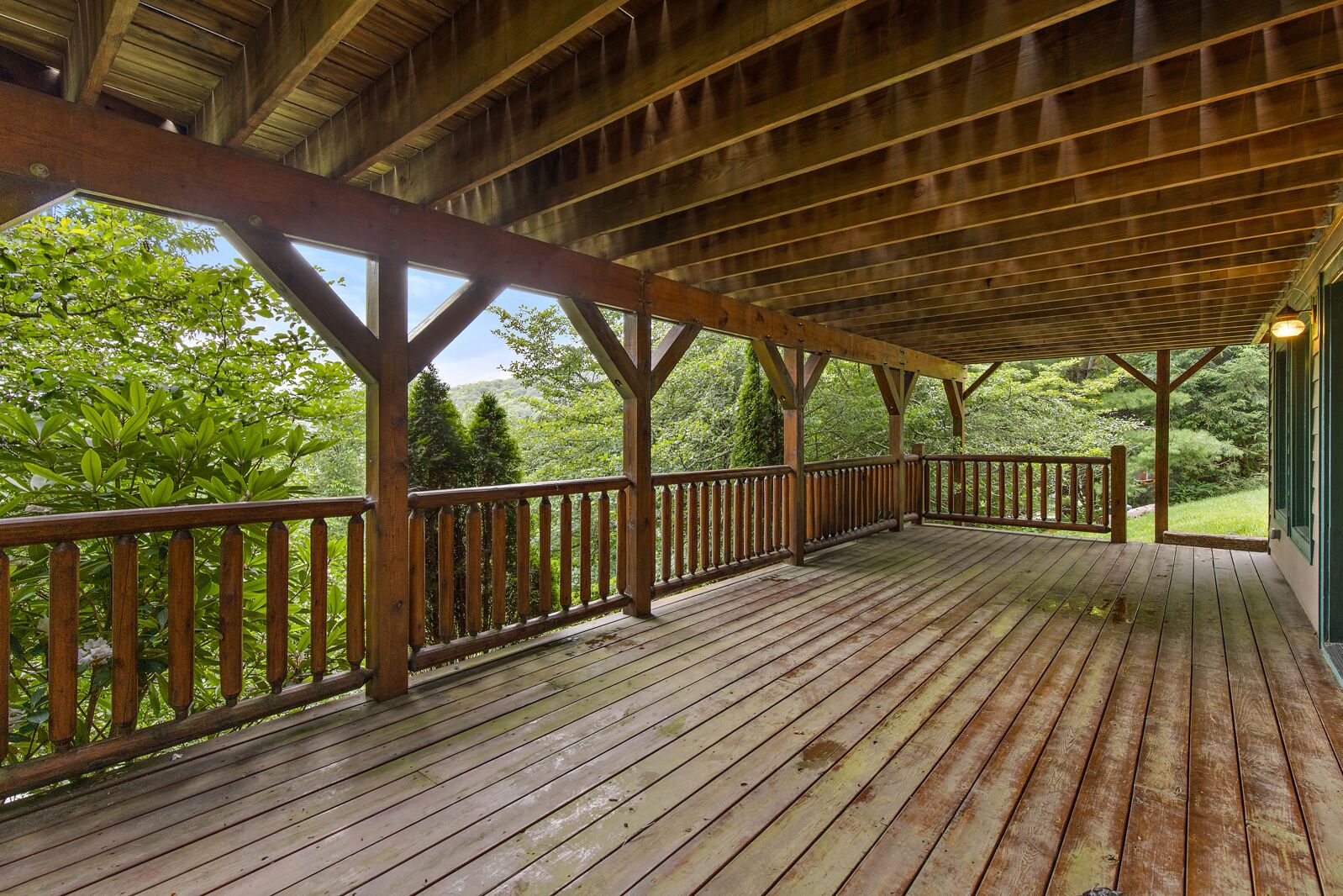 Une terrasse en bois dotée d’une rambarde, soutenue par des poutres et des colonnes en bois, qui offre une vue sur un paysage verdoyant et luxuriant.