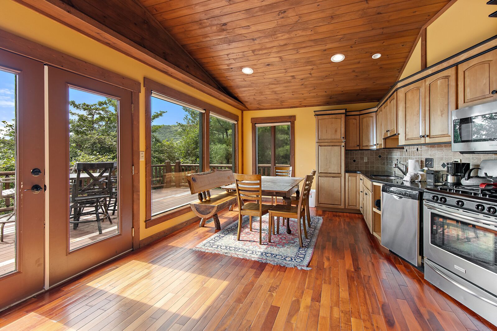 A spacious kitchen with wooden cabinets, a dining area with a wooden table and chairs, and large windows offering a view of the outdoors.