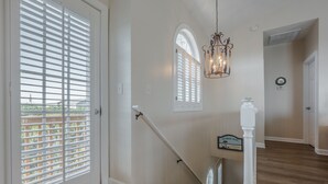 A staircase with a handrail, a chandelier, and a door with a window. - Callalily | Gorgeous Ocean Views in Topsail Beach! (Topsail Beach)
