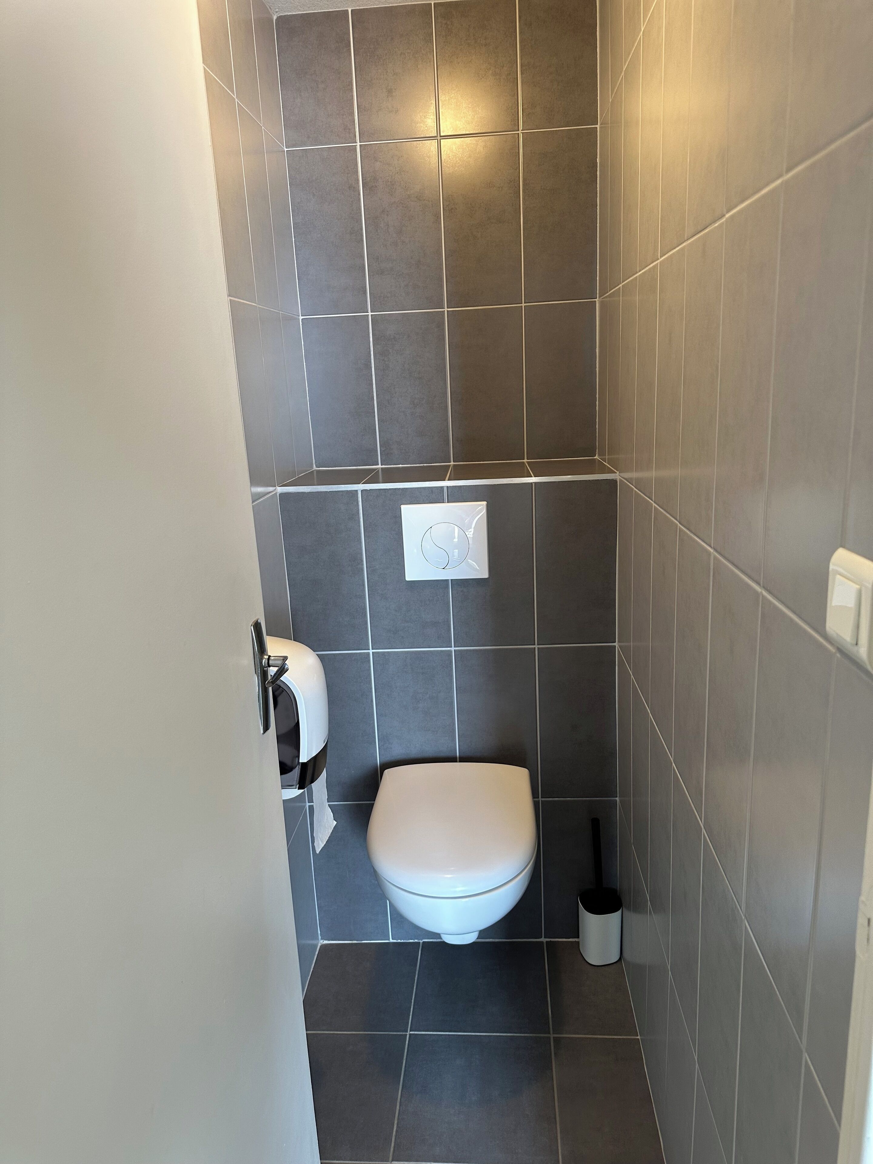 A small, modern bathroom with a toilet, a hand dryer, and a trash can.