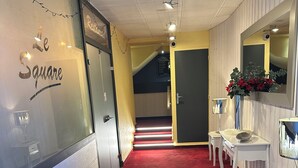 Un pasillo de hotel con alfombra roja, una recepción, un espejo y un cartel que dice 'Hotel Square'.