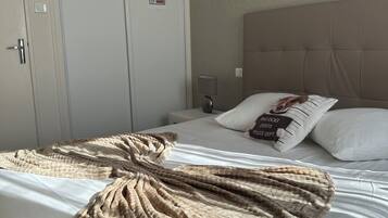 Quarto de hotel com cama, manta, travesseiro com pingente de coleira e mesa de cabeceira, além de luminária fixada na parede.