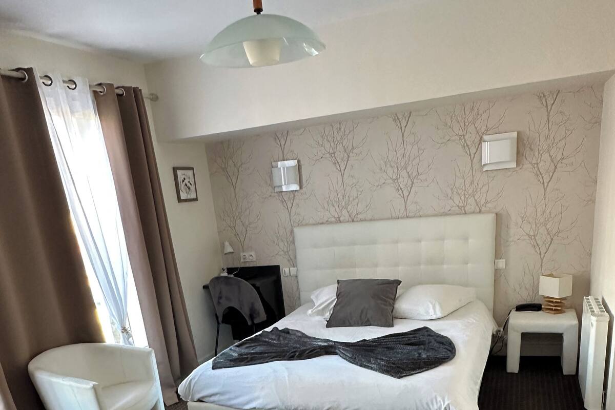 Une chambre d’hôtel avec un grand lit, une table de chevet, une chaise et une fenêtre avec des rideaux.