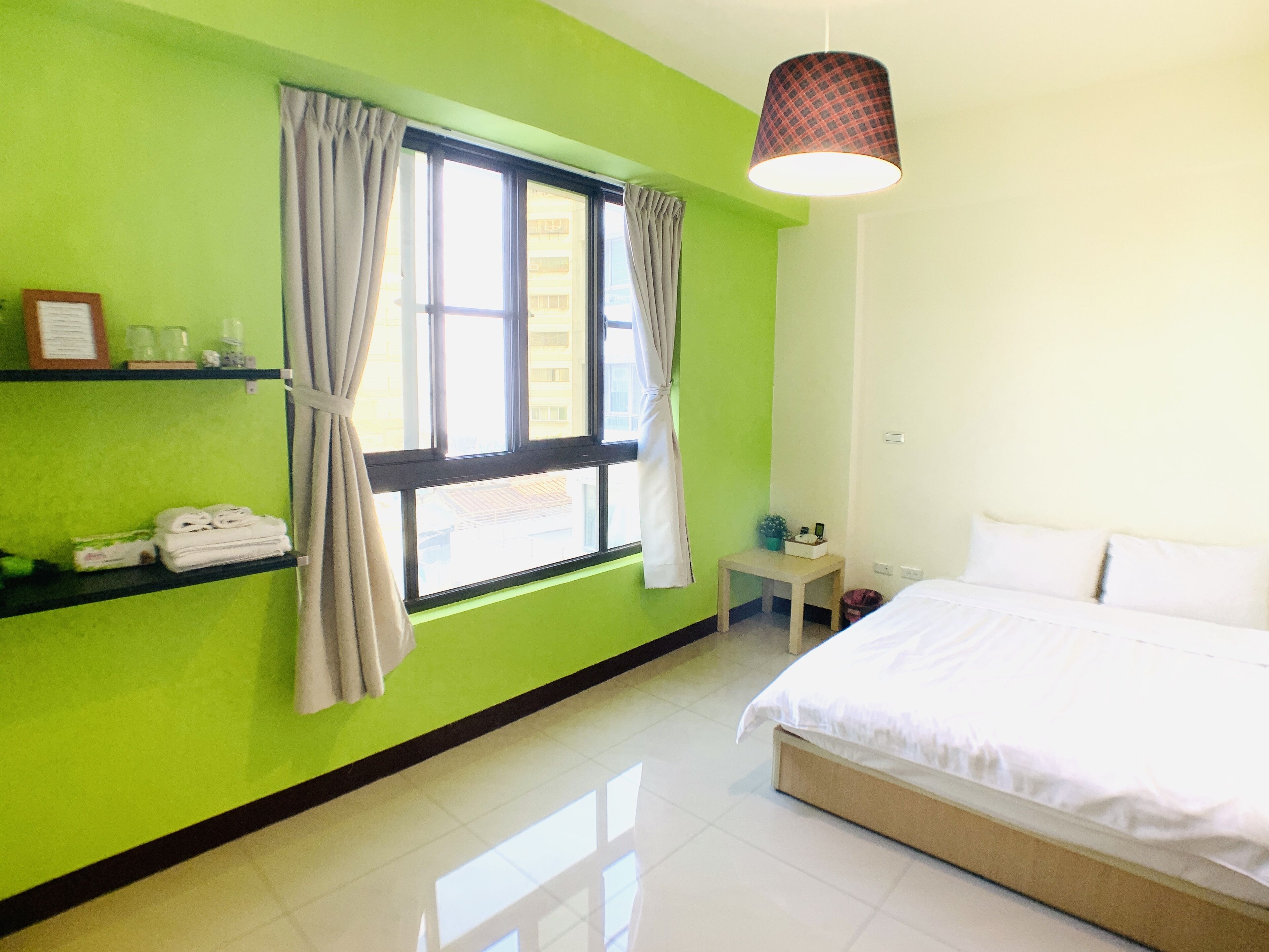 A hotel room with a large bed, a small table, a shelf with towels, and a window with curtains.