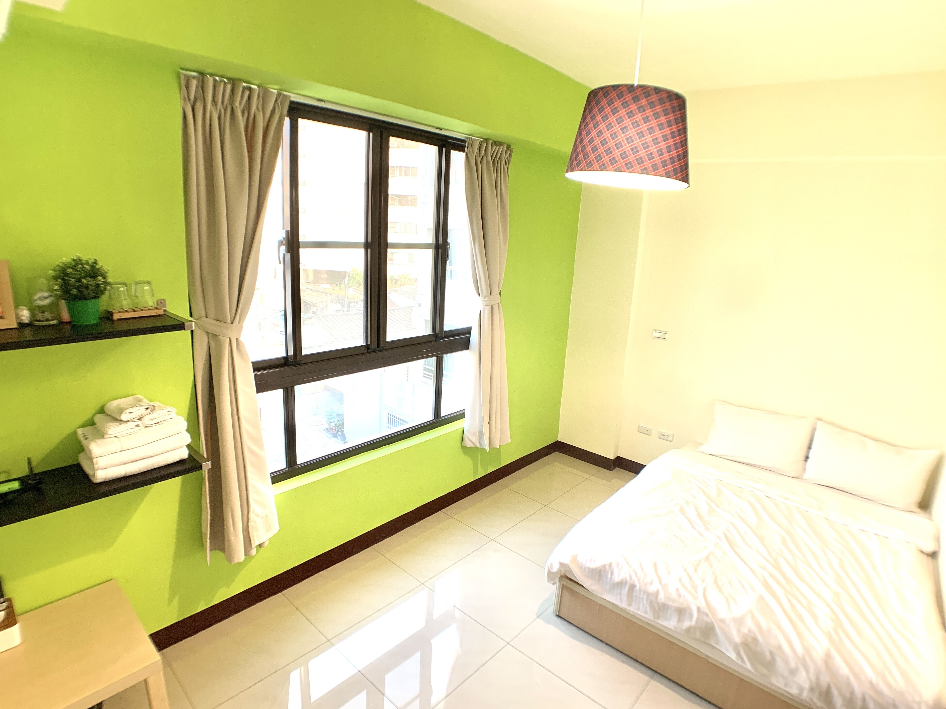 Una habitación con cama, ventana con cortinas, estante con toallas y una lámpara colgante.