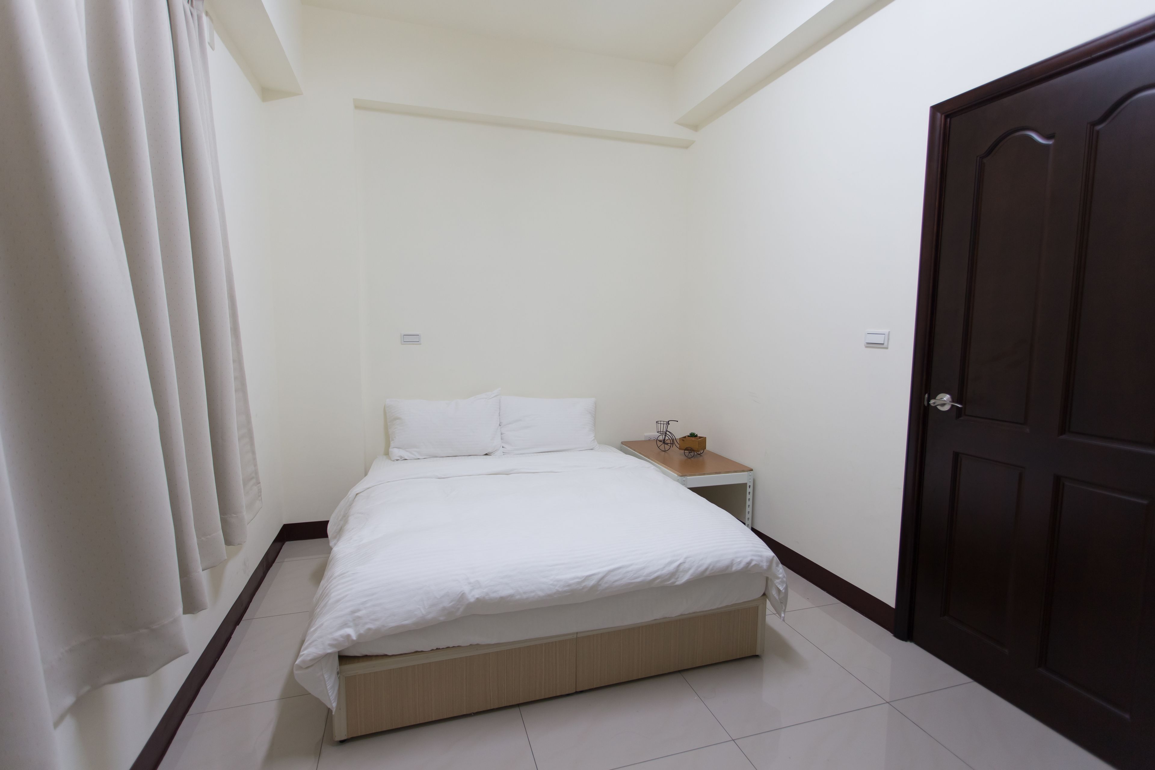 Una stanza piccola e pulita con un letto singolo, un comodino di legno e una porta in legno scuro.