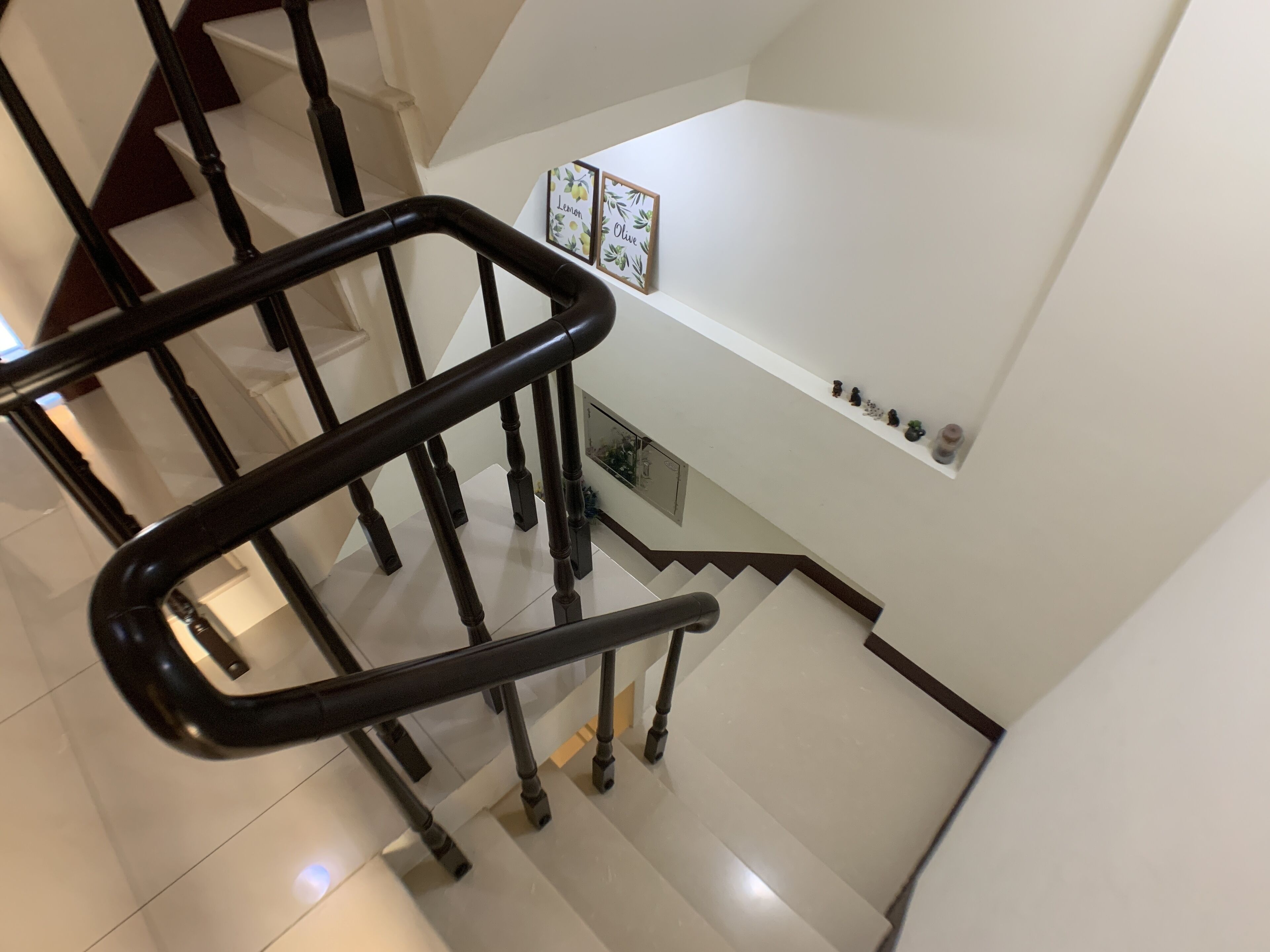 A modern staircase with a black handrail, white walls, and a small shelf with decorative items.