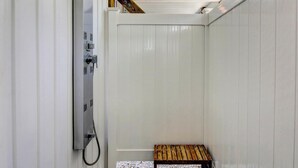Ein kleiner, abgeschlossener Duschbereich mit einer Holzbank und einer an der Wand montierten Duschbrause.