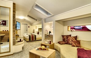 Habitació d'hotel moderna amb llit, sofà, taula de cafè i televisió.