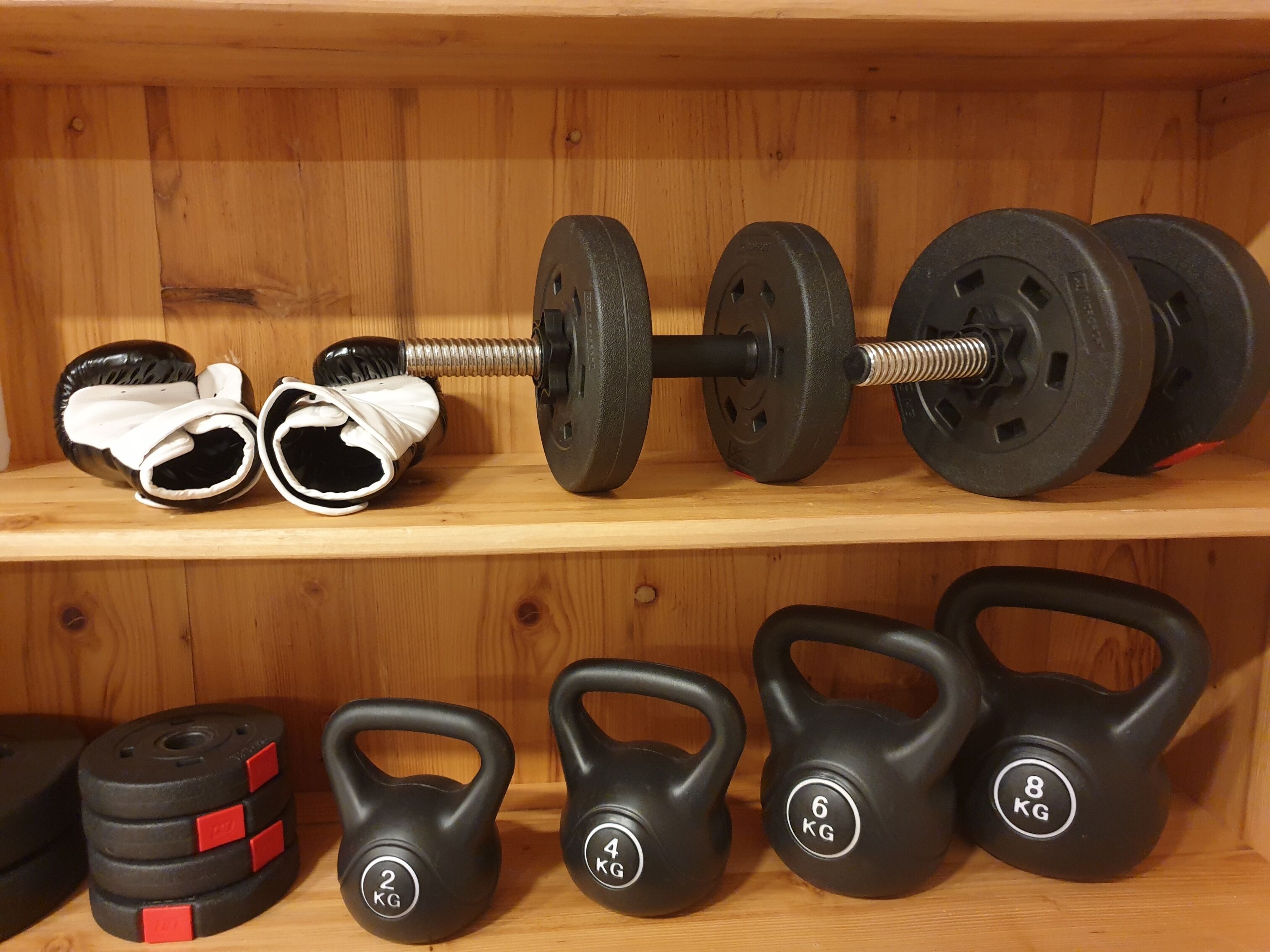 A wooden shelf with a barbell, weight plates, and kettlebells.