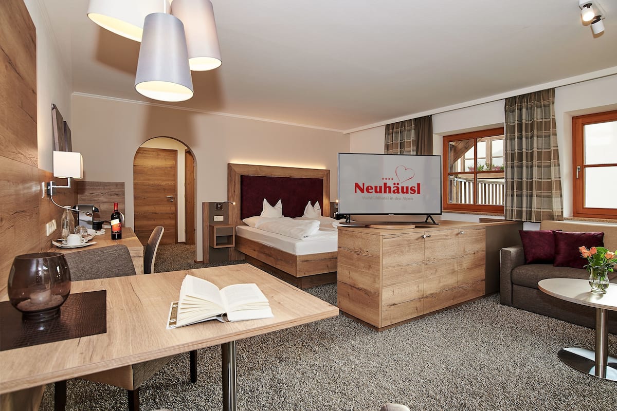 A modern hotel room with a bed, a desk, a sofa, and a television displaying the hotel name.