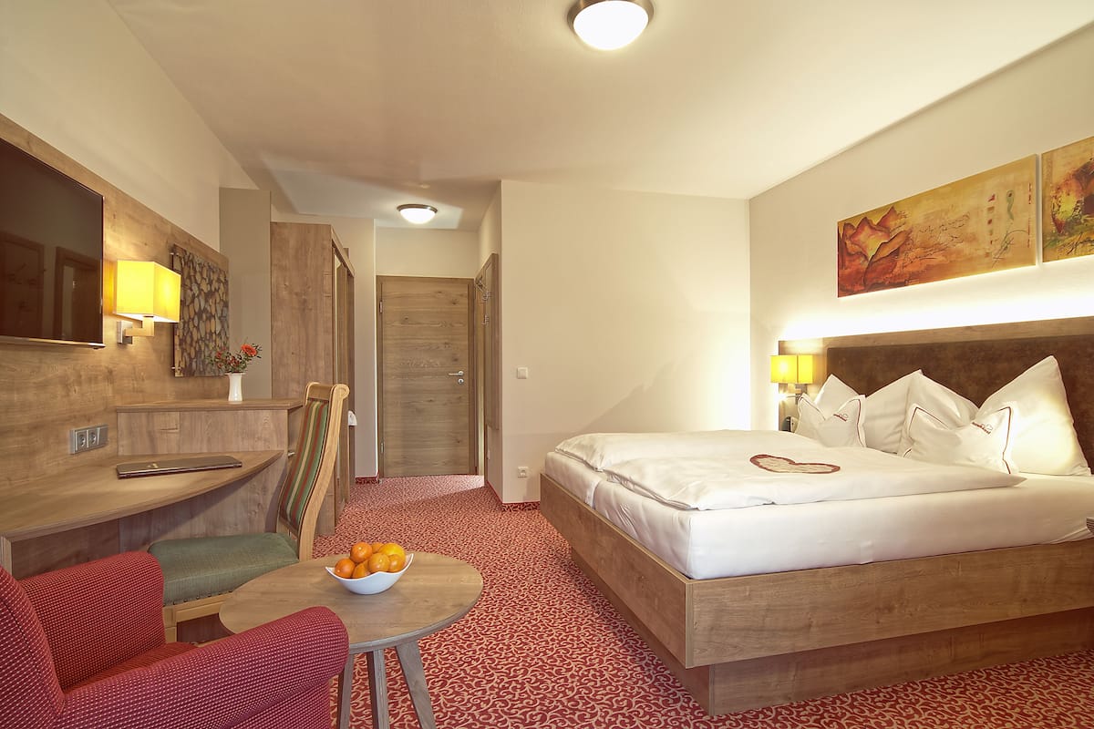 A hotel room with a bed, a small table with fruit, a chair, a desk, and a mirror.