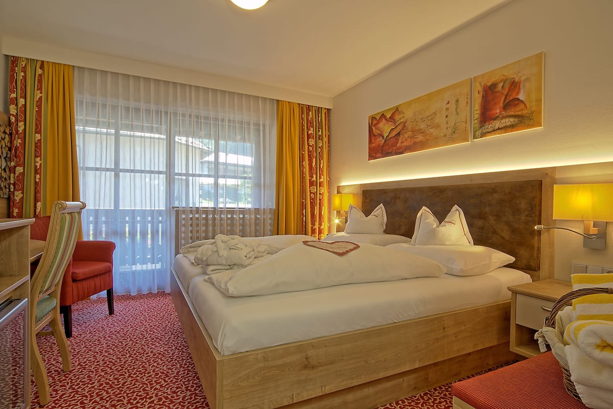 A hotel room with a large bed, a desk, a chair, and a window with curtains.