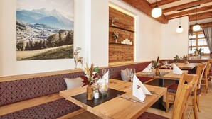 Un restaurante con mesas y bancos de madera, un cuadro de un extenso paisaje montañoso y vigas de madera en el techo.