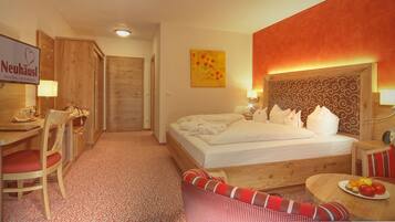 Une chambre d’hôtel avec un lit, un bureau, une chaise, une table à manger avec des fruits et une enseigne Neuhaus.