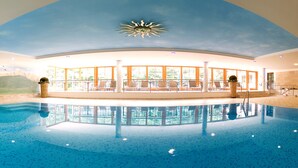 Una piscina interior con vista despejada del entorno circundante, que incluye sillones de descanso y un diseño de techo que simula el sol.
