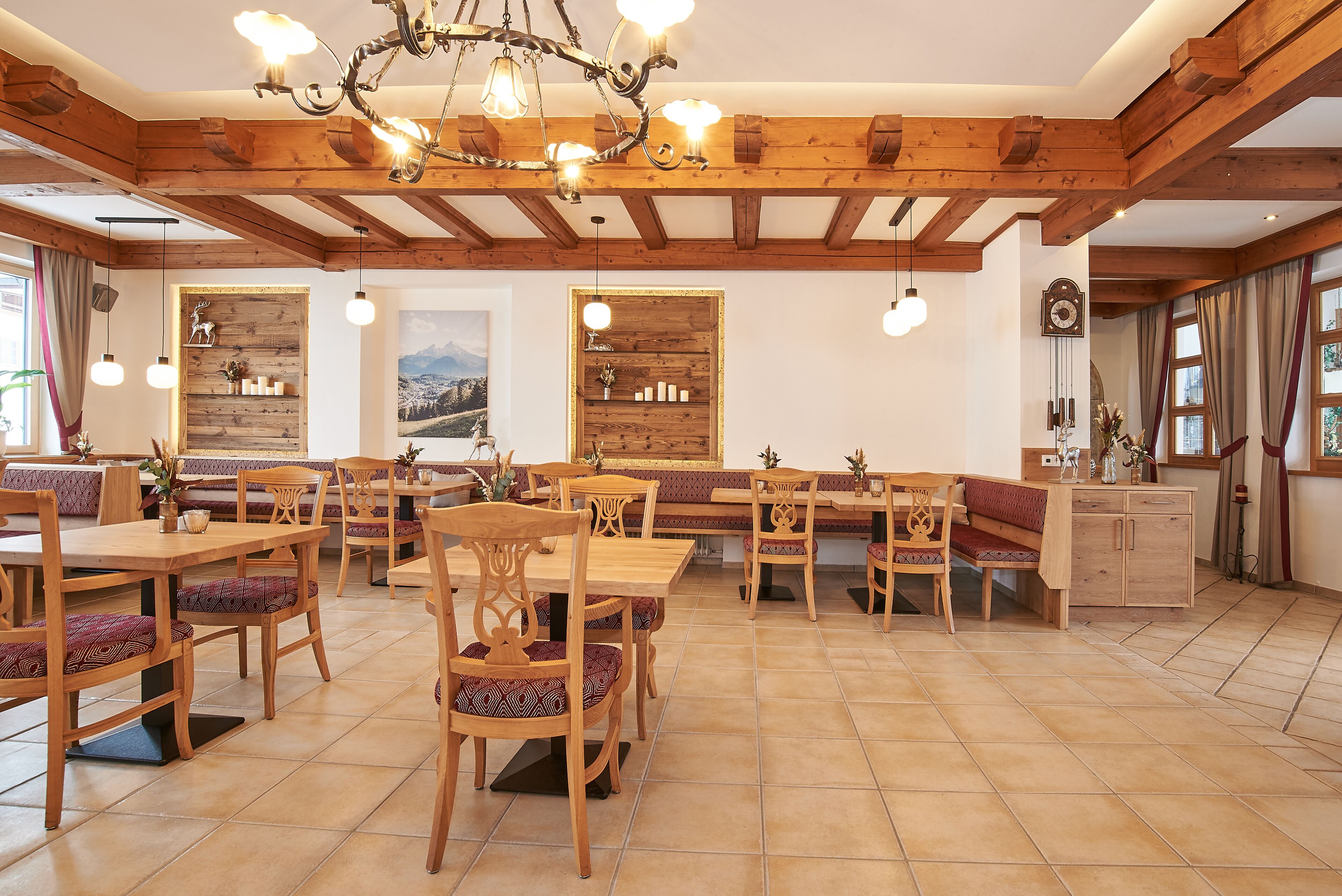 Ein Restaurant mit Holztischen und -bänken, einer Kristallleuchtre und einer Wanduhr.
