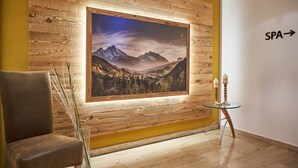Una habitación con una gran fotografía enmarcadas de un paisaje montañoso en la pared, una mesita con velas, y un cartel que indica el camino al spa.