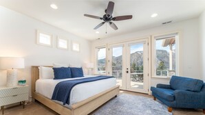 Une chambre à coucher avec un lit, une chaise bleue, un ventilateur de plafond et de grandes fenêtres.