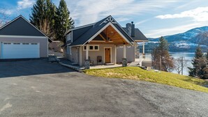 Une maison à deux étages avec un garage, une véranda et une vue sur un lac et des montagnes.