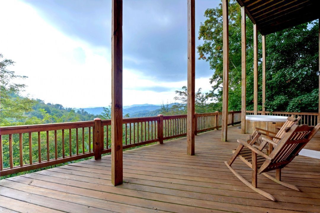 Une terrasse en bois, dotée d’une rambarde, d’une table et de chaises, qui offre une vue sur un paysage boisé.
