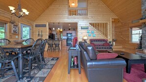 Une cabane en bois spacieuse comprenant un coin repas, un salon avec un canapé et une cuisine.